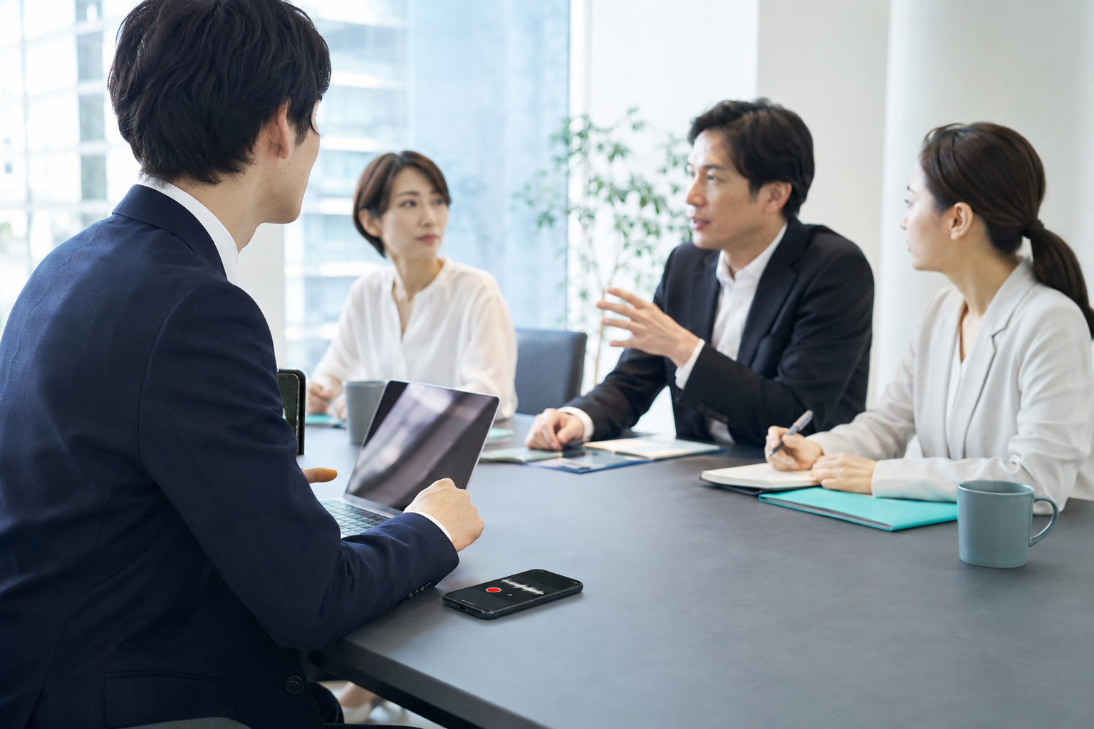 商談テーブルにスマートフォンを置いて会話を録音しながら、打ち合わせを進める営業担当者。